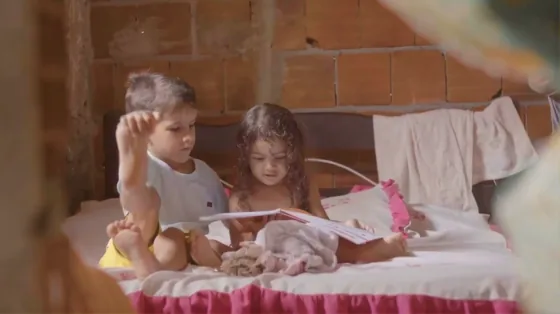 Duas crianças brincam sobre uma cama