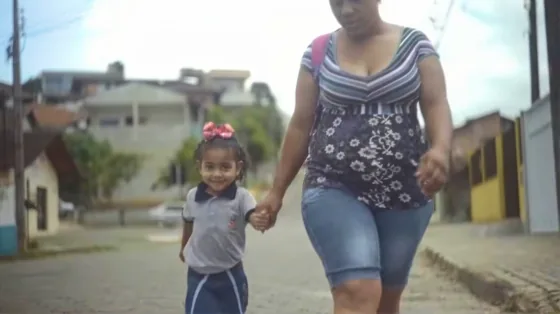 Mãe e filha caminham de mãos dadas pela rua