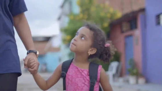 Menina de mochila olha para o adulto que segura sua mão