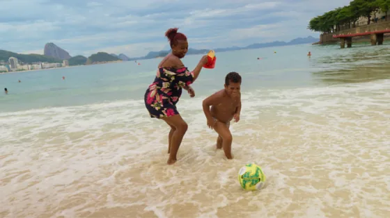 Avó e neto brincam com uma bola na beira do mar
