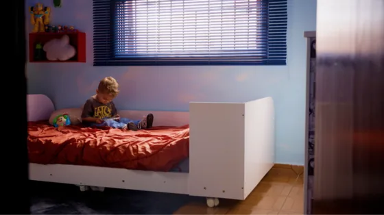 Criança sentada sozinha sobre a cama do quarto