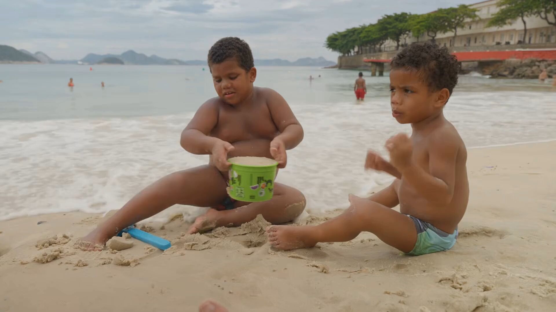 Duas crianças brincam com um balde na areia da praia