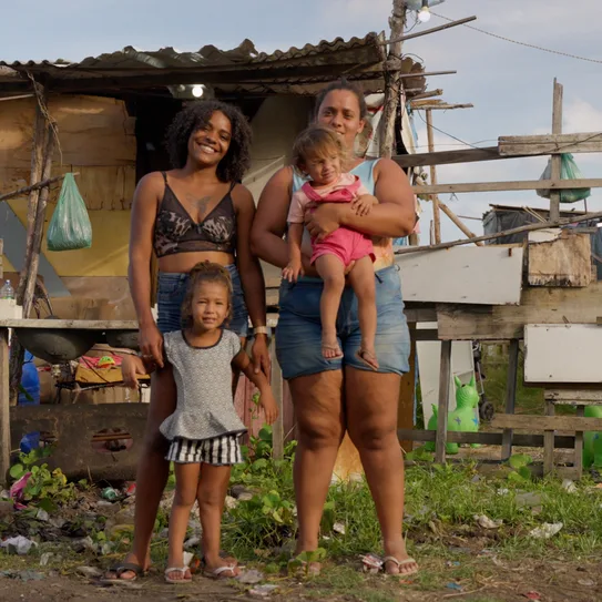 Duas mulheres com três crianças em frente a uma casa de madeira